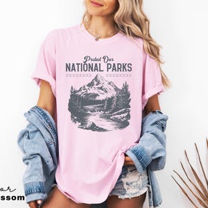 May include: A pink t-shirt with a graphic of a mountain range and a river. The text "Protect Our National Parks" is printed on the shirt.
