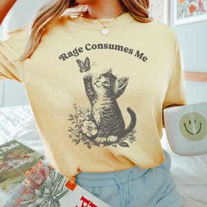 May include: A yellow t-shirt with the text "Rage Consumes Me" and a black and white illustration of a cat looking at a butterfly.