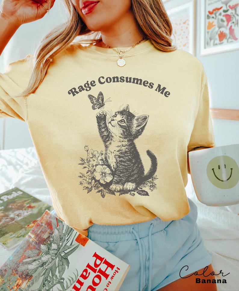 May include: A yellow t-shirt with the text "Rage Consumes Me" and a black and white illustration of a cat looking at a butterfly.