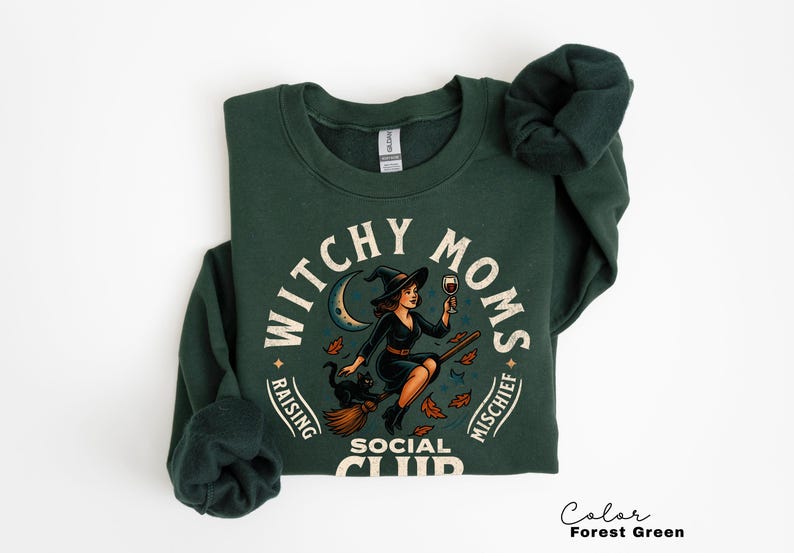 May include: Forest green sweatshirt with a graphic that reads "Witchy Moms Social Club". The design features a witch on a broom holding a glass of wine, with a black cat and crescent moon.