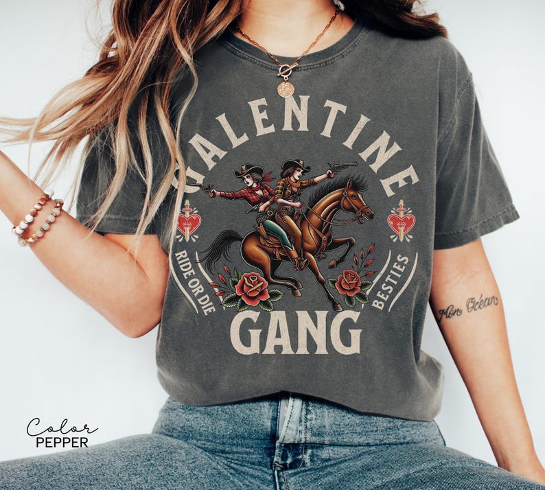 May include: Dark gray t-shirt with a graphic of two cowgirls riding a horse, guns drawn, surrounded by roses and hearts. The text reads "VALENTINE GANG, RIDE OR DIE, BESTIES".