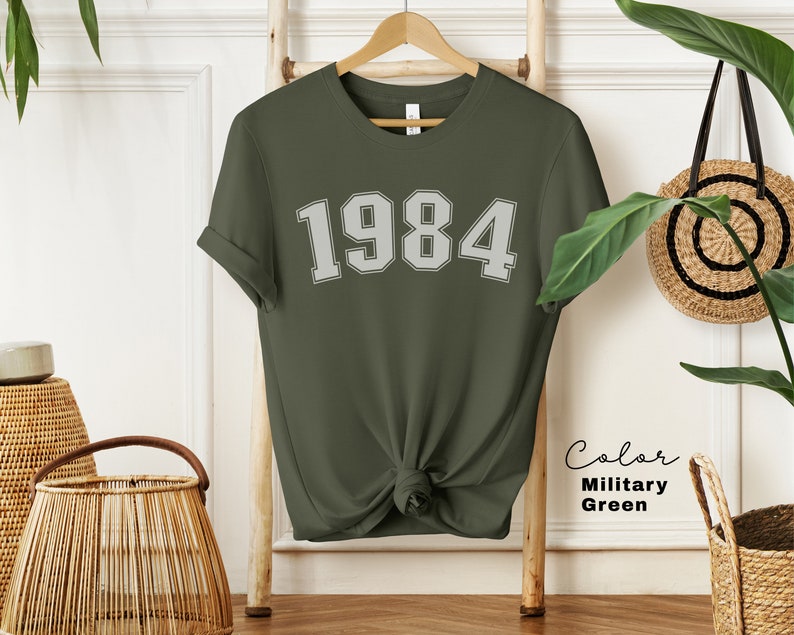 May include: A green t-shirt with the number 1984 printed in white on the front. The shirt is made of a soft, comfortable material and is perfect for everyday wear.