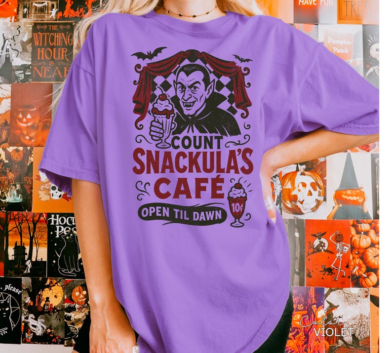 May include: A violet-colored t-shirt featuring a graphic of Count Snackula holding a milkshake. The design includes bats, a checkered curtain, and the text "COUNT SNACKULA'S CAFE OPEN TIL DAWN". A vintage-style ice cream cone is also shown.