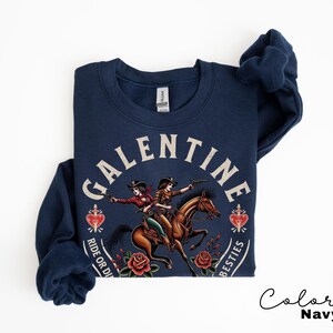 May include: Navy blue sweatshirt with a graphic featuring two cowgirls riding a horse, surrounded by roses and hearts. The text reads "GALENTINE" above and "RIDE OR DIE BESTIES" below. The color is navy.