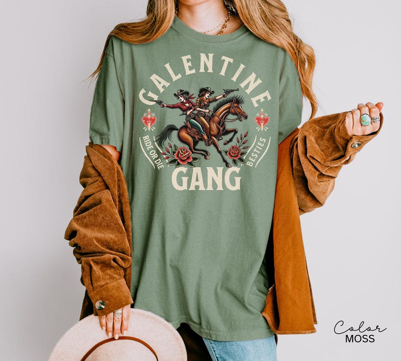 May include: Sage green t-shirt with a graphic of two cowgirls riding a horse, with the words "GALENTINE GANG" and "Ride or Die Besties". The shirt has a vintage, western aesthetic.