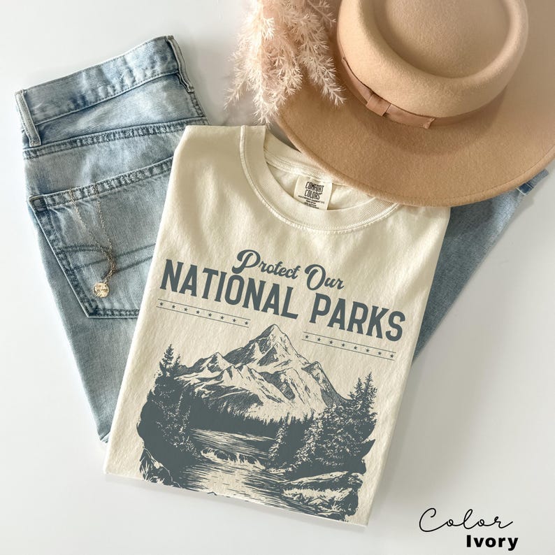 May include: Ivory colored t-shirt with a vintage style graphic of a mountain range and the text "Protect Our National Parks".