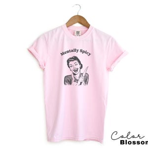 Puede incluir: Camiseta rosa con un gr&aacute;fico de una mujer sosteniendo un cuchillo y el texto "Mentally Spicy".