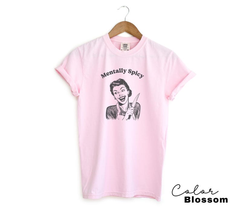 Puede incluir: Camiseta rosa con un gr&aacute;fico de una mujer sosteniendo un cuchillo y el texto "Mentally Spicy".