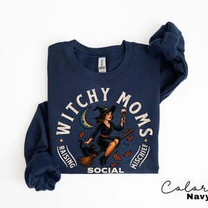 May include: Navy blue crew neck sweatshirt featuring a witch graphic with a black cat and the text "Witchy Moms Raising Mischief Social". The witch is holding a glass of wine. The sweatshirt is navy blue.
