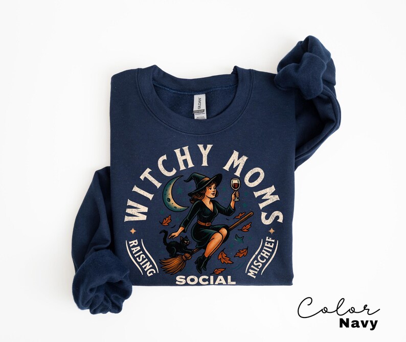 May include: Navy blue crew neck sweatshirt featuring a witch graphic with a black cat and the text "Witchy Moms Raising Mischief Social". The witch is holding a glass of wine. The sweatshirt is navy blue.