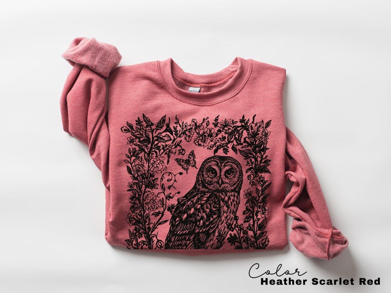 May include: Heather Scarlet Red sweatshirt with a black graphic of an owl surrounded by floral elements and butterflies. The text "Color Heather Scarlet Red" is at the bottom right.