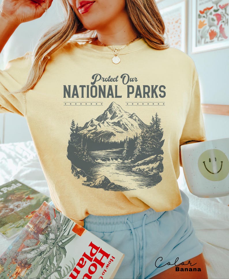 May include: A yellow t-shirt with a vintage-style graphic of a mountain range and a river. The text "Protect Our National Parks" is printed on the shirt.