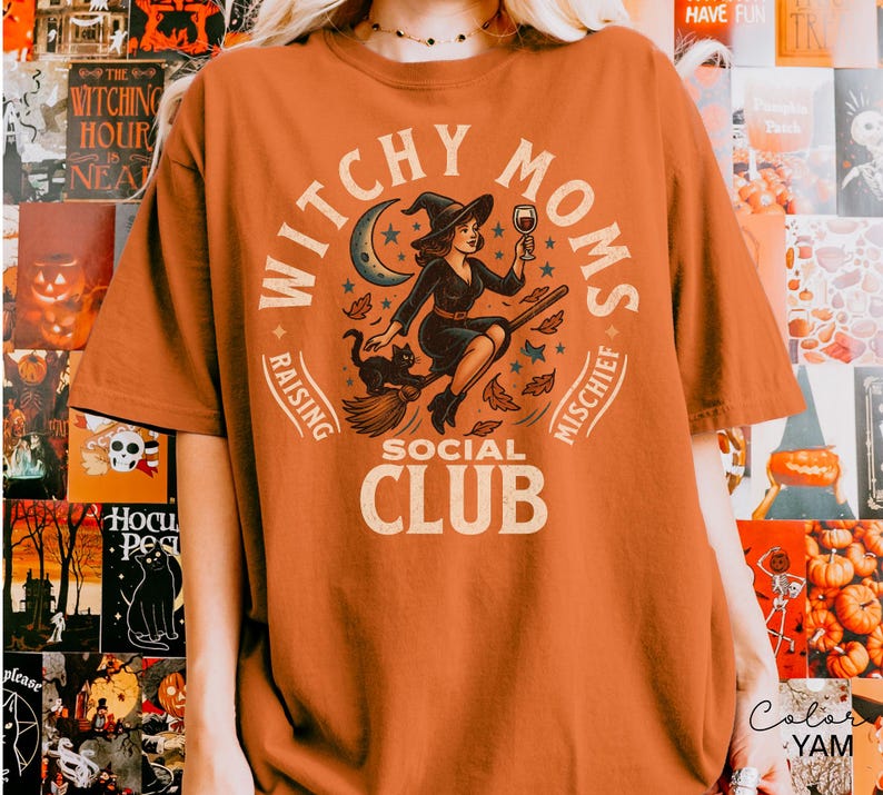 Puede incluir: Camiseta naranja con un dise&ntilde;o de una bruja en una escoba, un gato negro y las palabras "Witchy Moms Social Club". El dise&ntilde;o incluye una luna creciente, estrellas y hojas de oto&ntilde;o. La camiseta es un art&iacute;culo tem&aacute;tico de Halloween.