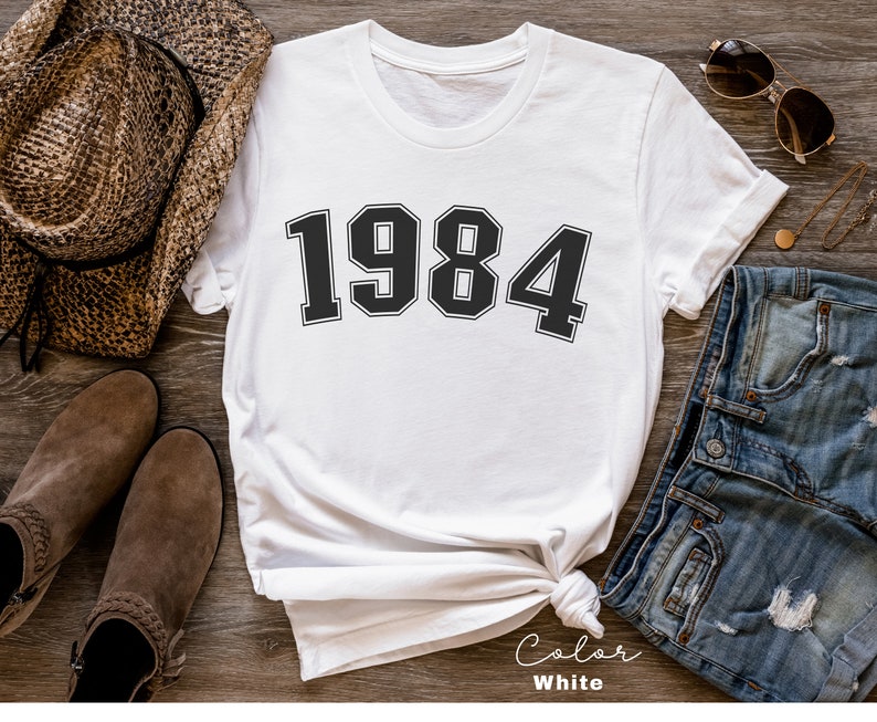 May include: White t-shirt with the year 1984 printed in black block letters.