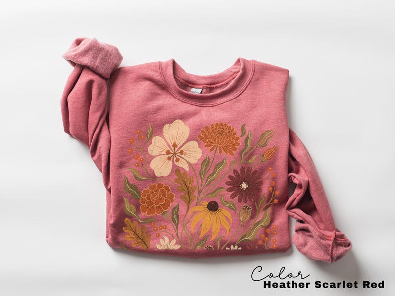 Puede incluir: Una sudadera de cuello redondo en color rojo escarlata jaspeado con un estampado gr&aacute;fico de varias flores en tonos crema, naranja, amarillo y marr&oacute;n oscuro con follaje verde. El texto "Color Heather Scarlet Red" aparece abajo a la derecha.
