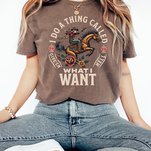 May include: A brown t-shirt featuring a graphic of a woman riding a horse. The text on the shirt reads "I do a thing called give 'em what I want".