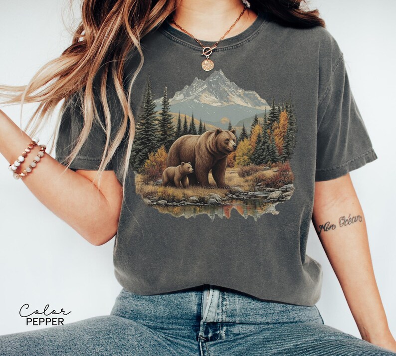 May include: Dark gray t-shirt featuring a detailed graphic of a bear and cub in a forest scene with a mountain backdrop. The image is printed on a comfortable, casual tee. The text "Color Pepper" is at the bottom.