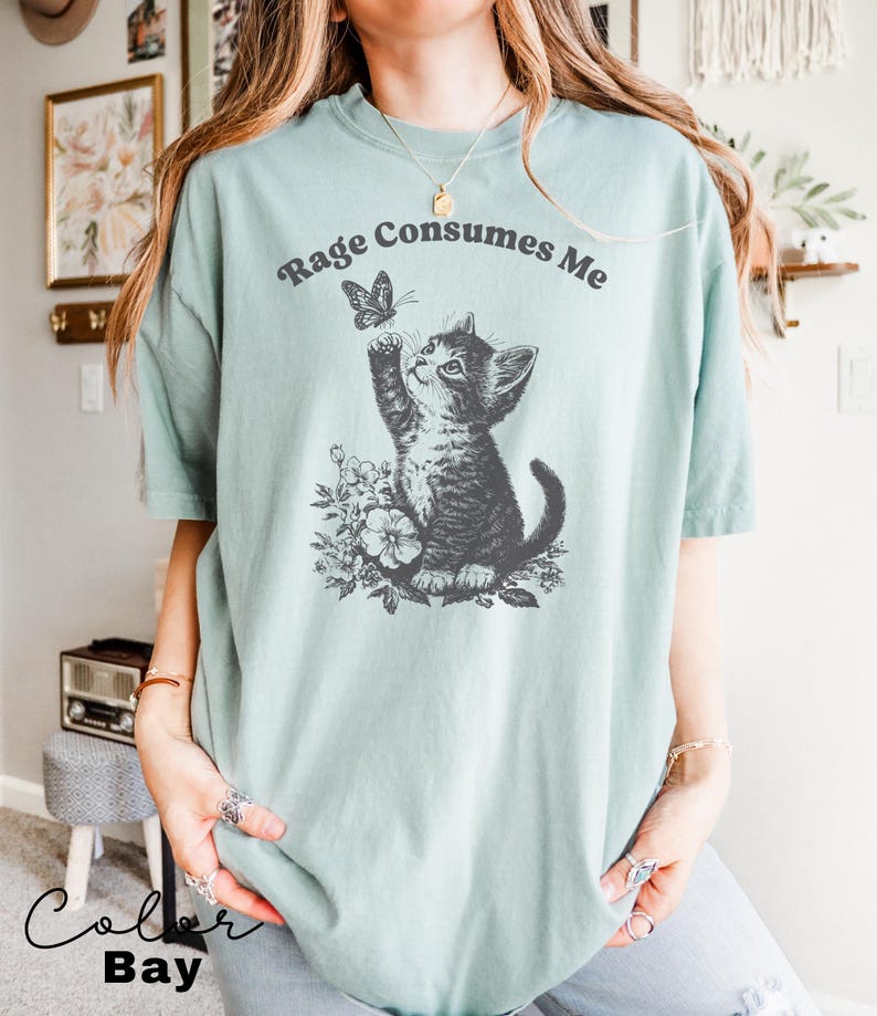 May include: A light blue t-shirt with a black and white illustration of a cat reaching for a butterfly. The text "Rage Consumes Me" is printed in black on the shirt.