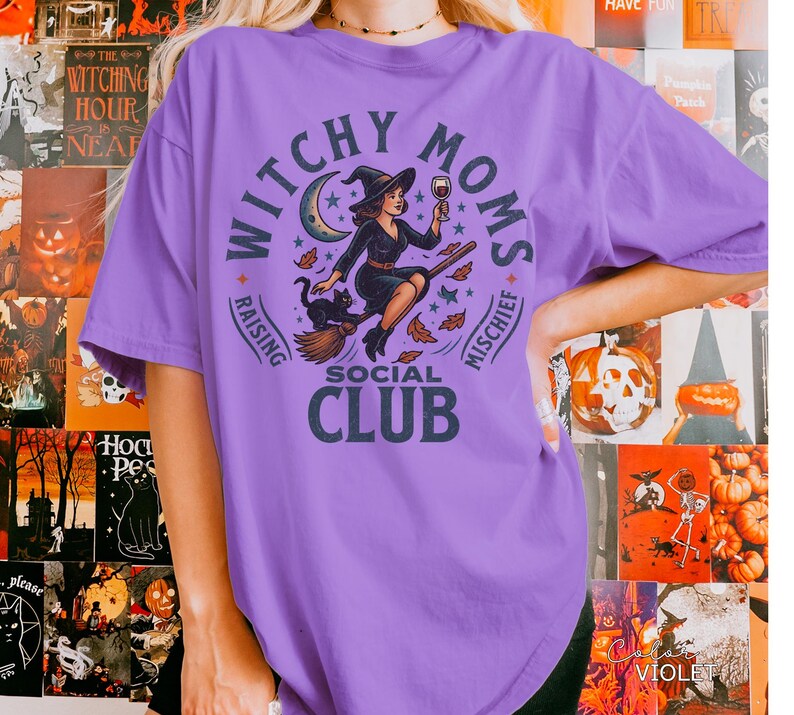 Puede incluir: Una camiseta de color lila con un dise&ntilde;o circular que dice "Witchy Moms Social Club". El dise&ntilde;o muestra una bruja en una escoba con un gato negro, una luna creciente y estrellas. Las palabras "Raising" y "Mischief" tambi&eacute;n est&aacute;n incluidas.