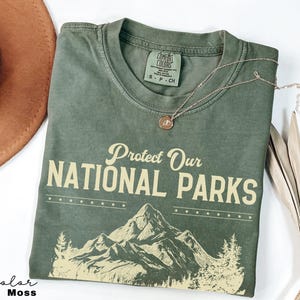 May include: A green t-shirt with the text "Protect Our National Parks" in yellow. The shirt features a graphic of mountains and trees in yellow.