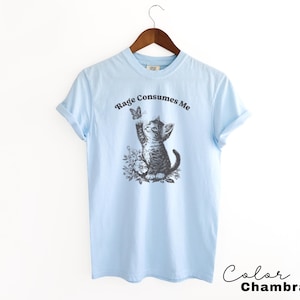 May include: Light blue t-shirt with a graphic of a kitten reaching for a butterfly. The text "Rage Consumes Me" is printed on the shirt.