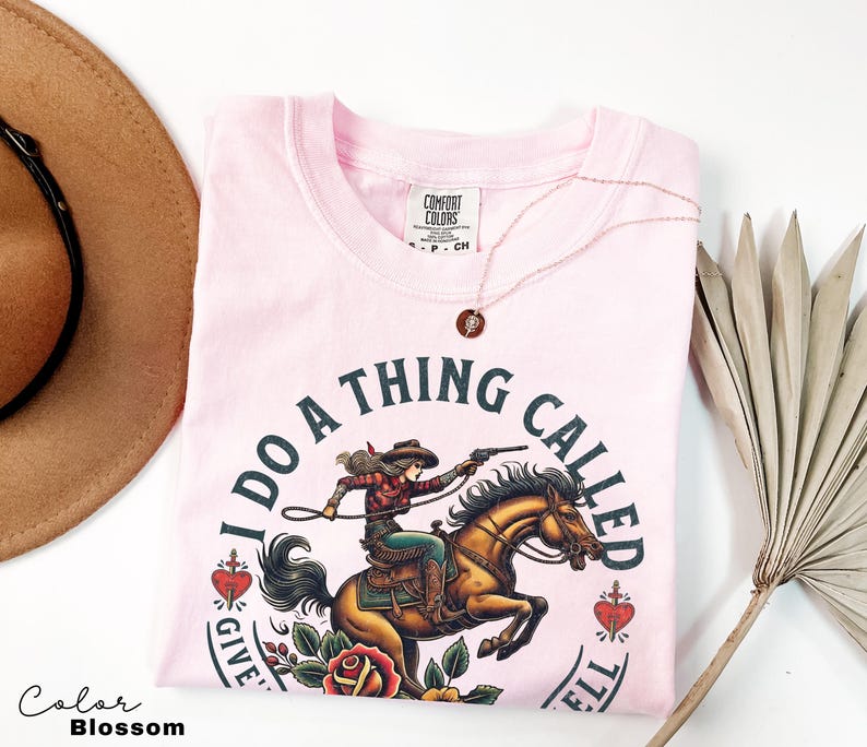 May include: Pink t-shirt featuring a graphic of a woman riding a horse with the text "I do a thing called give 'em hell".