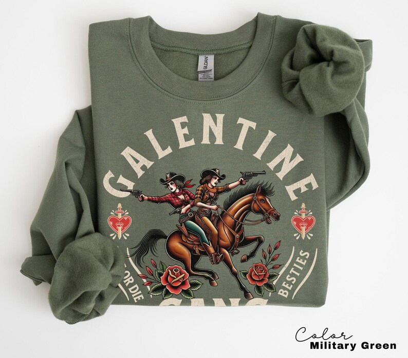 May include: Military green sweatshirt with a graphic featuring two cowgirls riding a horse, holding guns, and the text "GALENTINE BESTIES FOR DIE". The design includes roses and a heart.