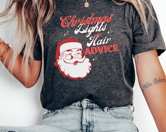 Op de afbeelding: Een donkergrijs T-shirt met een rode en witte illustratie van de kerstman. De tekst "Christmas Lights and Hair Advice" is in rood op het T-shirt gedrukt.