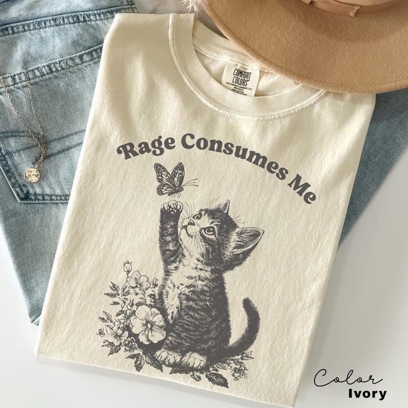 May include: Ivory colored t-shirt with the text "Rage Consumes Me" and a black and white illustration of a kitten looking up at a butterfly.