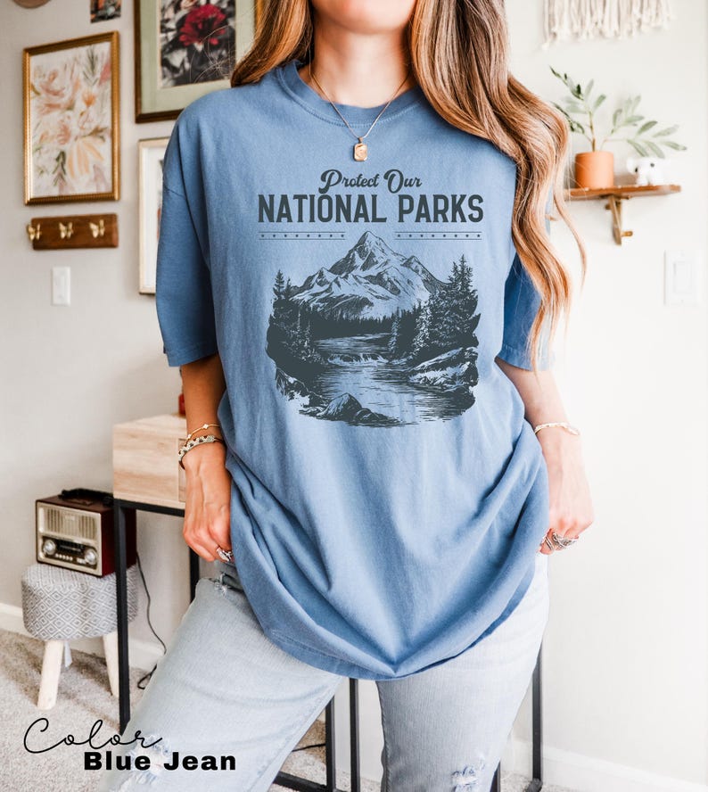 May include: A blue jean t-shirt with a graphic of a mountain range and a river. The text "Protect Our National Parks" is printed on the shirt.
