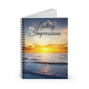 May include: A spiral bound notebook with a sunset over the ocean as the background. The text "Lasting Impressions" is written in a cursive font on the cover.