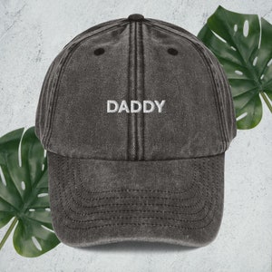 May include: A black vintage-style baseball cap with the word "DADDY" embroidered in white on the front.