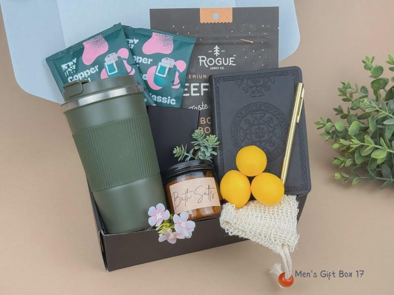 Puede incluir: Una caja de regalo que contiene un vaso de viaje verde oliva mate, un diario negro con un bol&iacute;grafo dorado, un frasco peque&ntilde;o con la etiqueta Bath Salts, tres esferas amarillas, una bolsa de malla peque&ntilde;a, dos paquetes verde azulado con la etiqueta Copper y un paquete de Rogue Jerky Co.