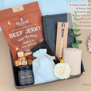 Puede incluir: Una caja de regalo que contiene una bolsa de cecina Rogue de arce y az&uacute;car moreno, un cuaderno de cuero negro, un bol&iacute;grafo de madera natural, calcetines beige, un tarjetero de cuero, una vela de salvia y c&iacute;tricos y tres caramelos en una bolsa.
