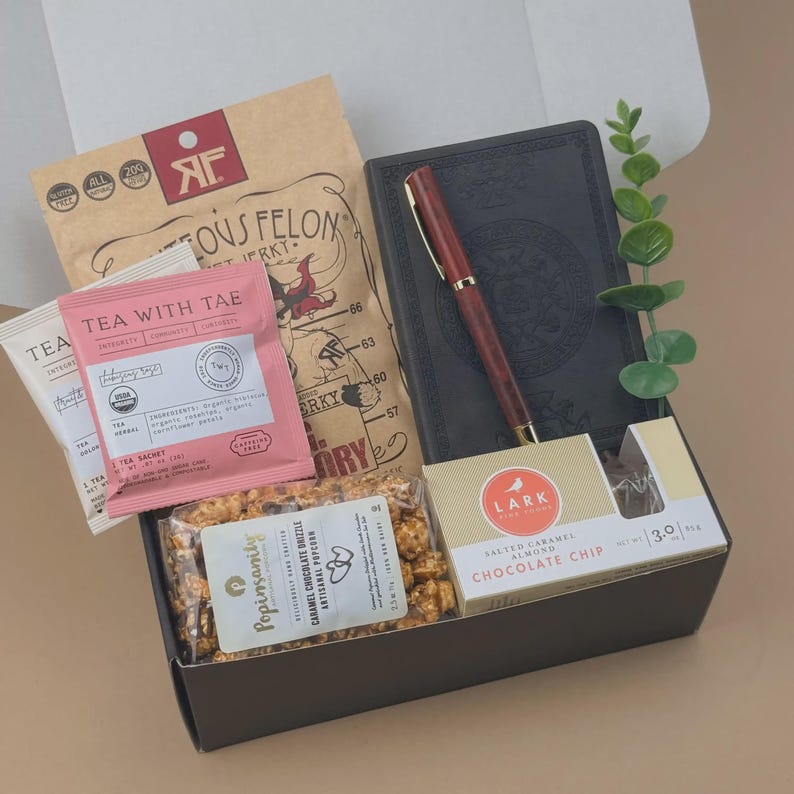 Puede incluir: Una caja de regalo que contiene una bolsa de cecina Righteous Felon, un diario negro con un bol&iacute;grafo rojo, un sobre de t&eacute; Tea With Tae rosa, palomitas de caramelo y chocolate Popinsanity, galletas Lark y una peque&ntilde;a rama verde.