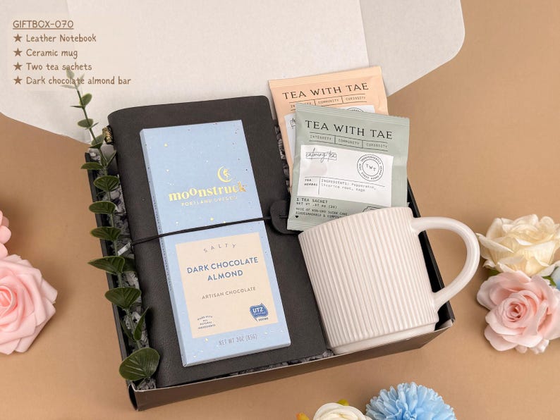 Puede incluir: Una caja de regalo que contiene un cuaderno de cuero negro, una barra de chocolate negro con almendras Moonstruck azul claro, una taza de cer&aacute;mica blanca acanalada y dos bolsitas de t&eacute; Tea With Tae. La caja incluye una lista llamada GIFTBOX-070.