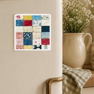 Könnte beinhalten: Quadratischer Magnet mit einem Patchwork-Quilt-Design. Die Quiltquadrate sind in verschiedenen Farben gehalten, darunter Rot, Blau, Gelb und Rosa. Der Magnet ist an einer weißen Kühlschranktür befestigt.