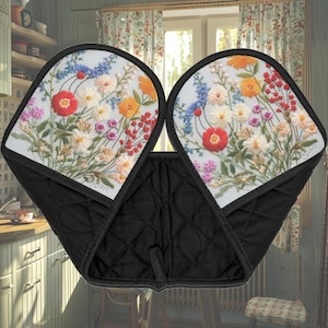 May include: A pair of black quilted oven mitts with a floral embroidered design. The mitts feature a white background with colorful flowers in shades of red, orange, yellow, pink, and blue. The mitts are designed for kitchen use.