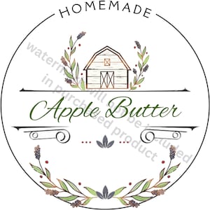 Op de afbeelding: Een witte cirkel met een zwarte rand en de tekst "HOMEMADE" bovenaan. Binnen de cirkel is een gestileerde illustratie van een schuur in groen en bruin met een krans van groene bladeren en paarse bloemen eromheen. De tekst "Apple Butter" staat in groen onder de schuur.