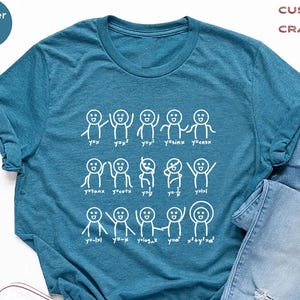 May include: A teal heather t-shirt with a white graphic of stick figures and mathematical equations. The shirt is paired with light blue jeans and white sneakers. The text "CUSTOM CRAFTERY" is in the upper right corner.
