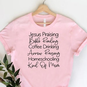 May include: Pink t-shirt with black text that reads "Jesus Praising, Bible Reading, Coffee Drinking, Arrow Raising, Homeschooling Kind of Mom".