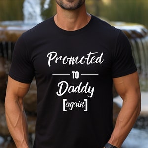 May include: Black t-shirt with white text that reads "Promoted to Daddy [again]"