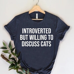 May include: A dark blue t-shirt with white text that reads "Introverted but willing to discuss cats".