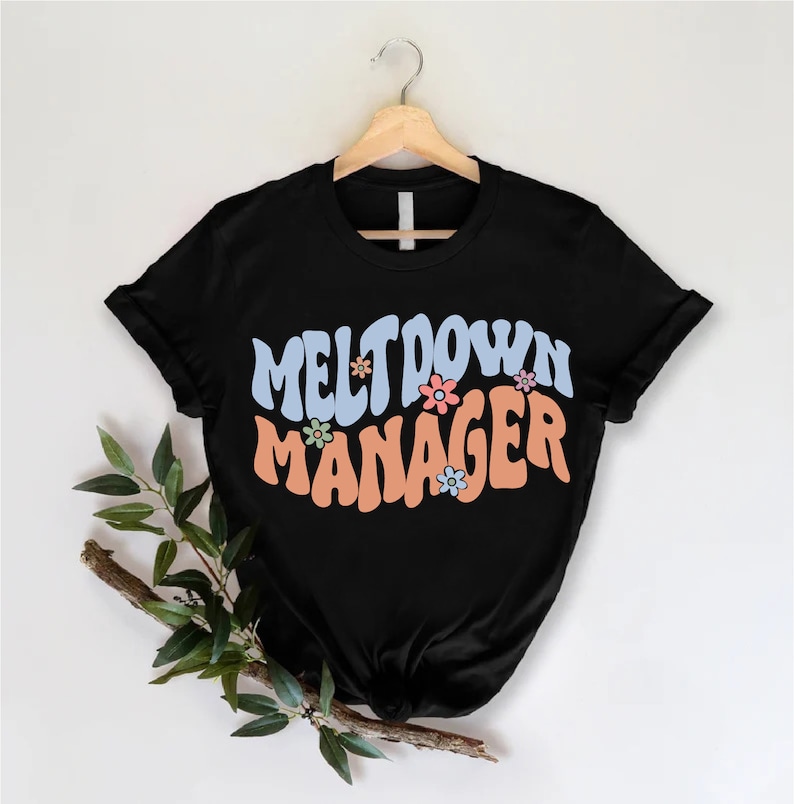 May include: Black t-shirt with the text "Meltdown Manager" in a retro font with colorful flowers.