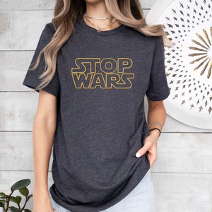 May include: A dark grey t-shirt with the text "STOP WARS" in a yellow outline.