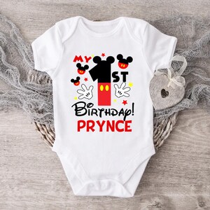 Puede incluir: Un body blanco para beb&eacute; con un dise&ntilde;o de Mickey Mouse rojo y negro. El body dice "My 1st Birthday! PRYNCE".