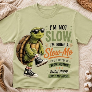 Puede incluir: Una camiseta verde claro con el gráfico de una tortuga verde con gafas de sol negras y zapatillas altas negras y blancas. El texto dice: I'M NOT SLOW, I'M DOING A SLOW-MO, LIFE'S BETTER IN SLOW MOTION, RUSH HOUR ISN'T MY HOUR.