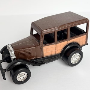 May include: A brown and tan vintage toy car with black tires and silver rims. The toy car has a detailed design, including windows and a textured roof. The car is a classic model, likely from the early 20th century.