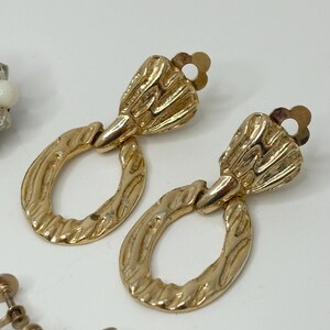 May include: A pair of gold tone clip-on earrings with a textured oval design and a decorative top.