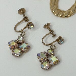 May include: A pair of gold tone clip-on earrings with iridescent stones. The earrings have a cluster of stones in the shape of a flower.